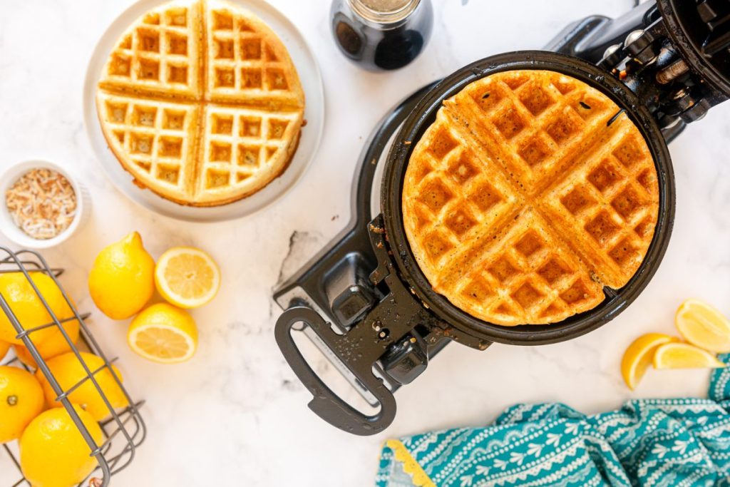 finished waffle in belgium waffle maker with another waffle on a plate nearby